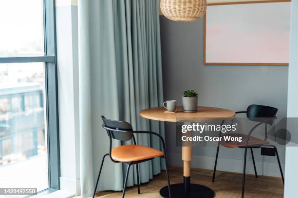 stylish wooden chair and table in the living room with potted plant and coffee mug - curtain hotel stock-fotos und bilder