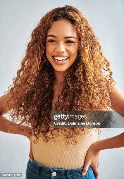 beleza, cabelo e moda com uma mulher em estúdio em um fundo cinza sentindo-se feliz com um sorriso e penteado encaracolado. rosto, bonito e rir com uma jovem atraente de pé mãos nos quadris dentro - alongamento de cabelo - fotografias e filmes do acervo