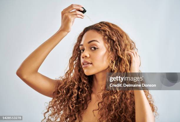 black woman, beauty and hair care with serum dropper for treatment and repair against a grey studio background. beautiful african female model in haircare with cosmetic oil pipette for healthy scalp - etherische olie stockfoto's en -beelden