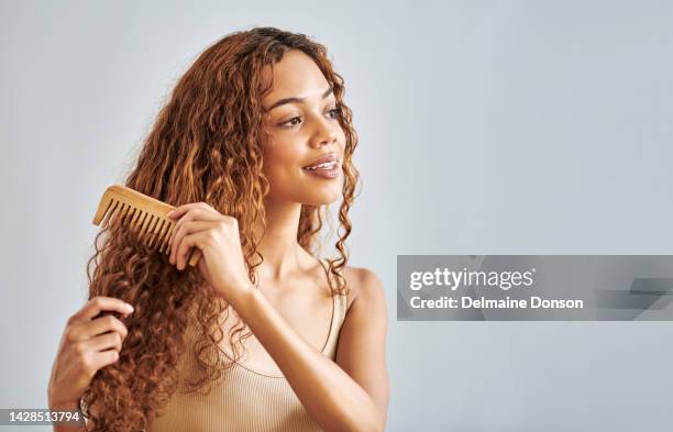 beauté, cheveux et brosse avec une femme brossant sa coiffure bouclée en studio sur un fond gris avec maquette. visage, soins capillaires et peigne avec une jolie jeune femme peignant ses belles boucles - hair curls photos et images de collection