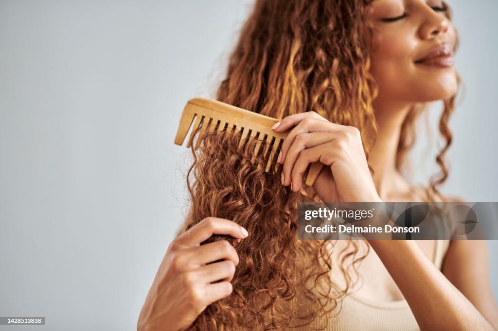 Haarpflege, Schönheit und Frau, die ihr lockiges Haar während ihrer Selbstpflegeroutine mit einem Holzkamm bürstet. Schönes, junges und hispanisches Mädchen, das ihre sauberen natürlichen Schlösser in einem Studio mit Kopierraum durchkämmt.