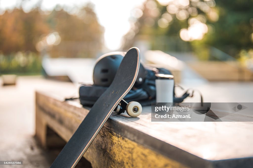 Skateboard, das sich auf eine Bordsteinbox mit Kaffeetasse und Helm darauf stützt