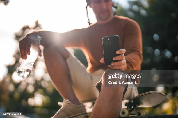 relaxed biracial man on skateboard making a video call with smart phone - active lifestyle stock pictures, royalty-free photos & images