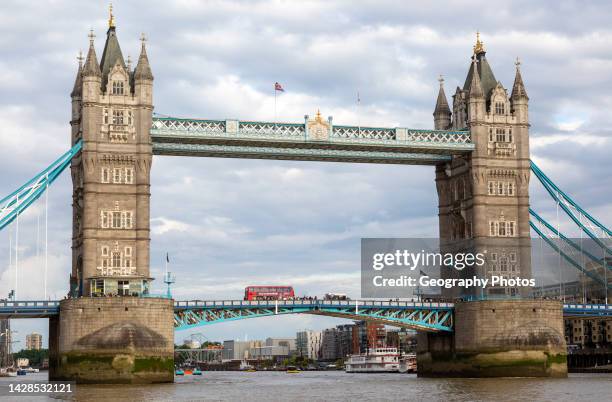 Red double decker bus crossing Tower Bridge, River Thames, London, England, UK.