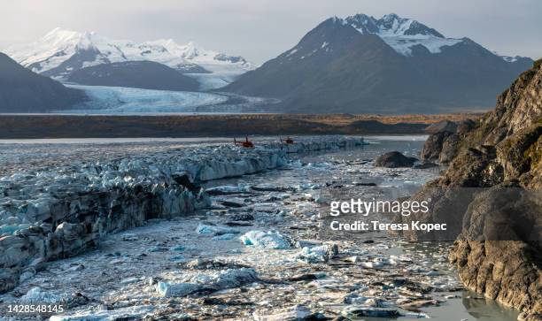 edge of knik glacier where it becomes a lake in alaska with red helicopters in distance and icebergs - knik glacier stock pictures, royalty-free photos & images