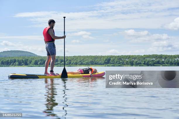 the father rolls his daughter on a paddle board. - paddle board men imagens e fotografias de stock