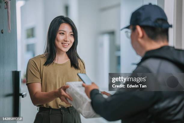 asiatische chinesin erhält lieferpaket, die den empfang der hauszustellung auf dem smartphone unterzeichnet - asien e commerce stock-fotos und bilder