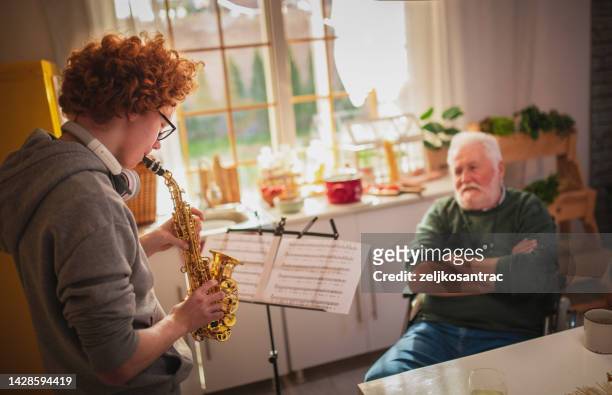 happy senior man and grandson having fun while playing saxophone at home - saxophone player stock pictures, royalty-free photos & images