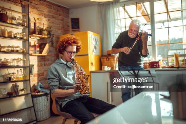 glücklicher älterer mann und enkel, der spaß hat, während er zu hause saxophon und geige spielt - saxophone stock-fotos und bilder