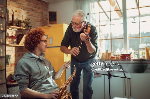 happy senior man and grandson having fun while playing saxophone  and violin at home - jonge senioren in groep stockfoto's en -beelden