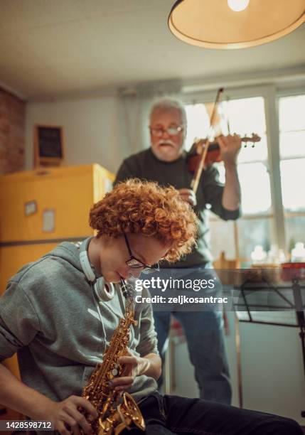 glücklicher älterer mann und enkel, der spaß hat, während er zu hause saxophon und geige spielt - music band stock-fotos und bilder