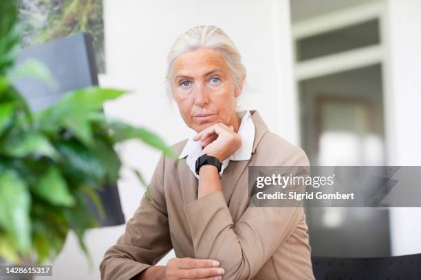 portrait of mature businesswoman sitting at desk in office - une seule femme d'âge mûr photos et images de collection