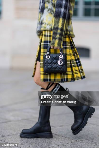 Alexandra Lapp wears total look Dior, yellow blue checkered v neck jumper, skirt with slit, black shorts, Lady Dior bag, boots, knee high socks with...