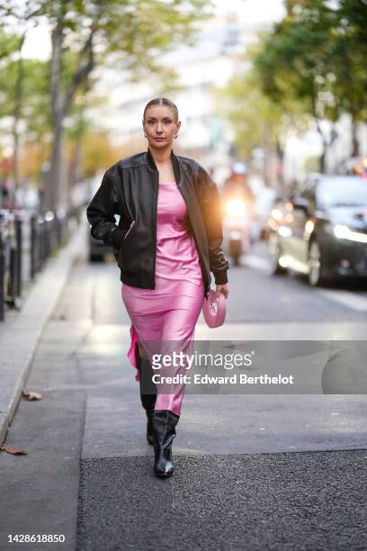 Justyna Czerniak wears a black bomber jacket, a pink silky lustrous midi slit dress, a black leather knee-high boots, a pink bag from Coperni,...