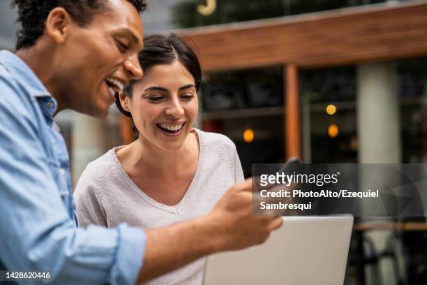 side shot african-american man and latin-american woman looking at a smartphone screen and laughing - klantbetrokkenheid stockfoto's en -beelden