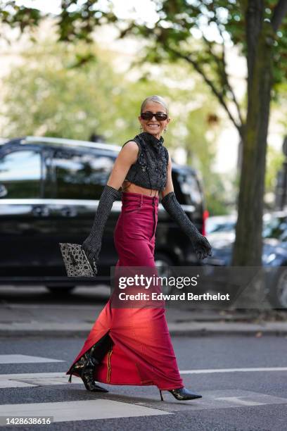 Caroline Daur wears sunglasses, earrings, a gray wool sleeveless / tank top / crop top, gray wool ribbed elbow length gloves, an Acne bag, a red...