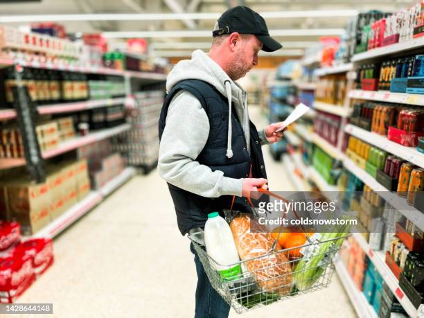 mid adult man looking at list in energy drink aisle of supermarket - monster energy stockfoto's en -beelden