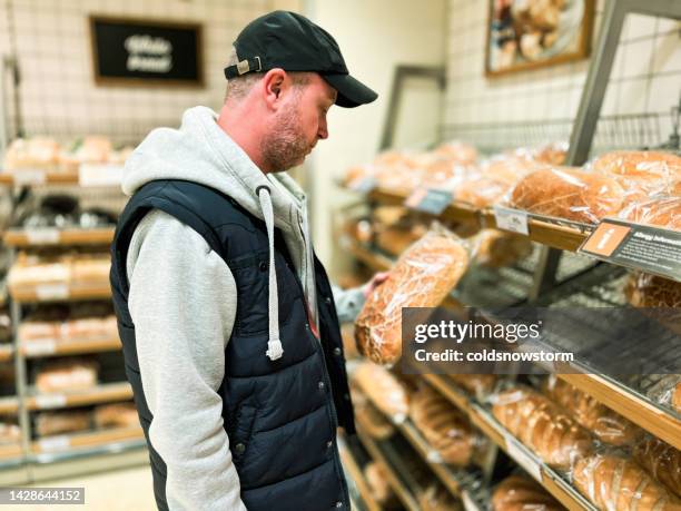 mittlerer erwachsener mann, der brot in der bäckereiabteilung des supermarktes betrachtet - brot einkaufen stock-fotos und bilder