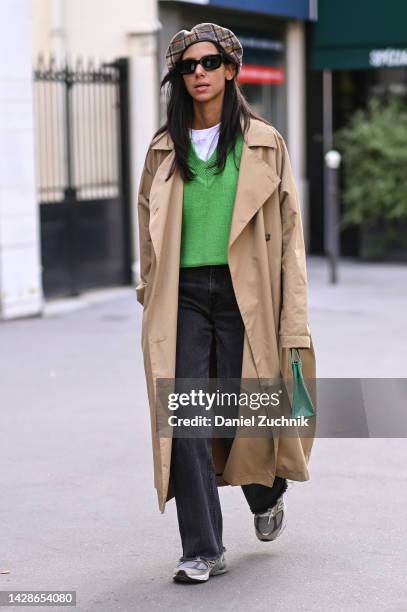 Guest is seen wearing a tan trench, green sweater, white shirt, black jeans, New Balance sneakers and a plaid hat outside the Dries Van Noten show...