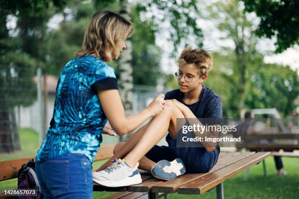 madre cuidando la pierna herida de su hijo con spray desinfectante - leg wound fotografías e imágenes de stock