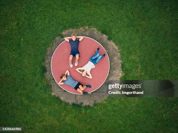 three kids enjoying resting on playground wheel carousel - draaimolen stockfoto's en -beelden
