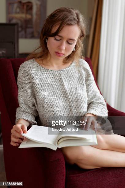 young woman rests and reads a book in an armchair. natural light - no pants day photos et images de collection