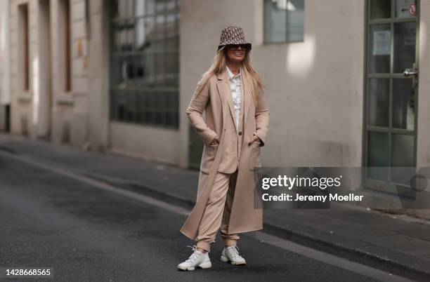 Martina Maturi is seen wearing brown Burberry sunglasses, beige/brown Dior bucket hat, white button shirt and suit from Gioia, beige long wool coat...