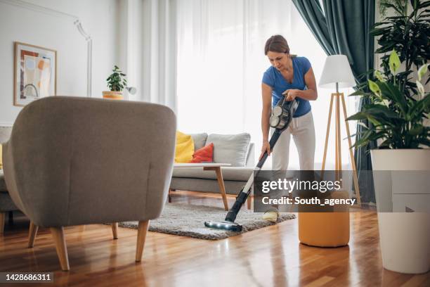 woman vacuuming the living room with cordless vacuum cleaner - vacuum cleaner woman stockfoto's en -beelden