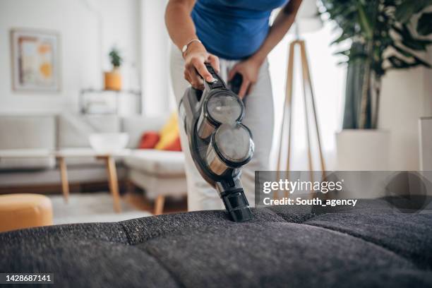 donna casalinga che aspira mobili in una casa con un aspirapolvere portatile portatile - aspirapolvere foto e immagini stock