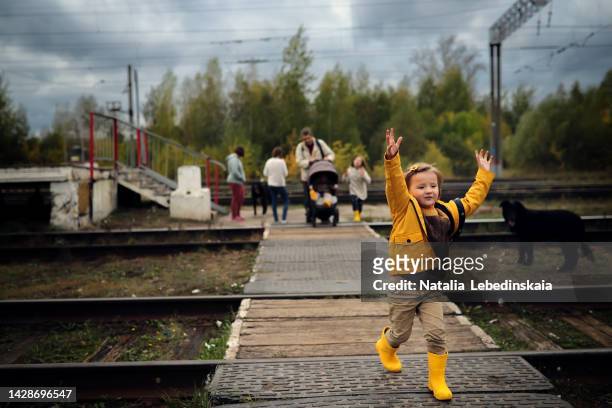 happy child in yellow wellies runs away from her family at a railway crossing in a rural area. - treincoupé stockfoto's en -beelden