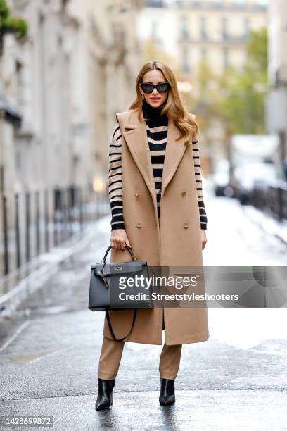 Alexandra Lapp wearing a beige sleeveless coat by Madeleine, a black and beide striped knitted turtleneck pullover by Madeleine, beige pants by...