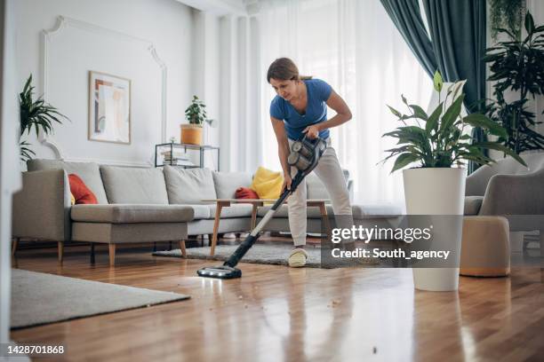 woman vacuuming the living room with cordless vacuum cleaner - cordless device stock pictures, royalty-free photos & images
