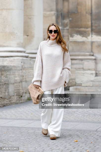 Alexandra Lapp wearing a cream colored oversized knitted turtleneck pullover by Simone Bruns, ivory colored wide leg pants by Giorgio Armani, a beige...