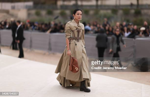 Yoyo Cao is seen wearing gold earrings, a beige long trench coat from Dior, a beige and brown corset, diamonds bracelets, a brown shiny leather Dior...