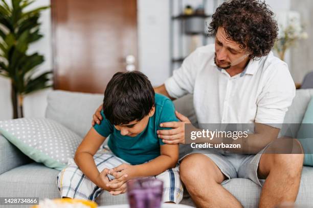 father talking comforting his sad son on the sofa - cyberbullying stock pictures, royalty-free photos & images