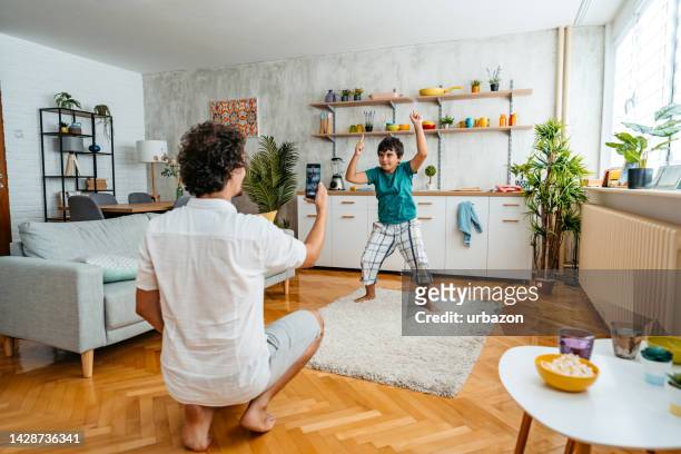 father filming his son dancing in the living room - photo sharing stock pictures, royalty-free photos & images