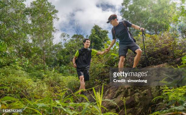 young caucasian man helping his  partner to reach the top of a mountain. - reaching higher stock pictures, royalty-free photos & images