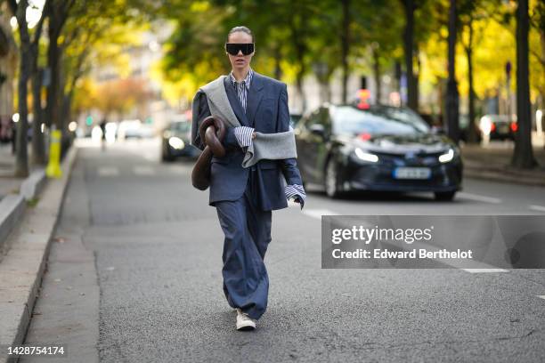 Guest wears black futurist sunglasses from Versace, a navy blue and white striped print pattern shirt, a gray oversized blazer jacket, matching gray...