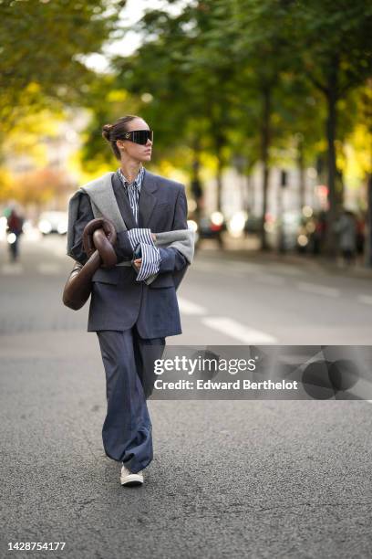 Guest wears black futurist sunglasses from Versace, a navy blue and white striped print pattern shirt, a gray oversized blazer jacket, matching gray...