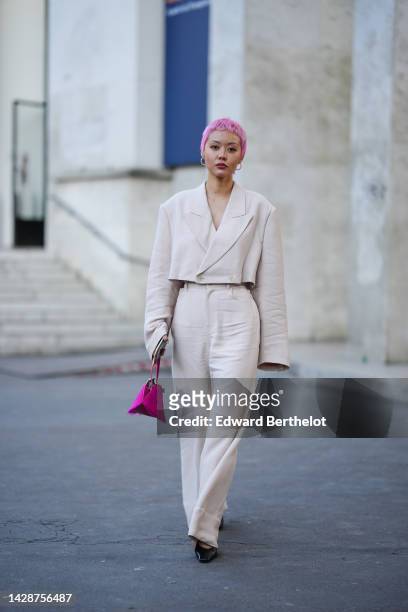 Guest wears pink earrings, a white latte cropped blazer jacket, matching white latte wide legs pants, a neon pink fur and shiny leather handbag,...