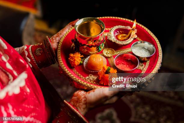 tradition indian woman holding a plate decorated with oil lamp, sweet food, flowers, and religious offering on the occasion of karwa chauth festival. - diwali decoration stock pictures, royalty-free photos & images