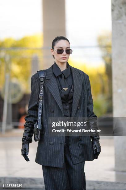 Guest wears black square sunglasses, a black shirt, a black striped print pattern oversized blazer jacket, matching black striped print pattern wide...