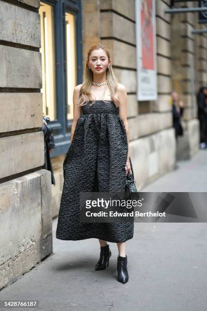 Guest wears silver and diamonds earrings, a white pearls necklace, a black embossed ruffled pattern shoulder-off / midi dress, a black leather with...