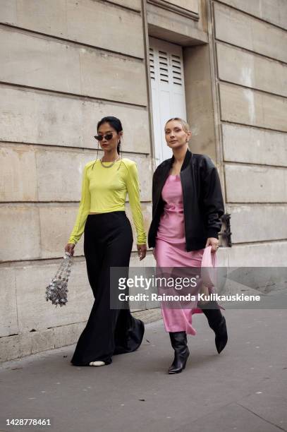 Pornwika Spiecker wearing a black maxi skirt, yellow/green long sleeve top, and grey bag, and Justyna Czerniak wearing a pink silk dress, black...