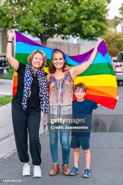 reifes lesbisches paar, das mit seinem sohn posiert und eine regenbogenfahne hält - regenbogenfahne stock-fotos und bilder