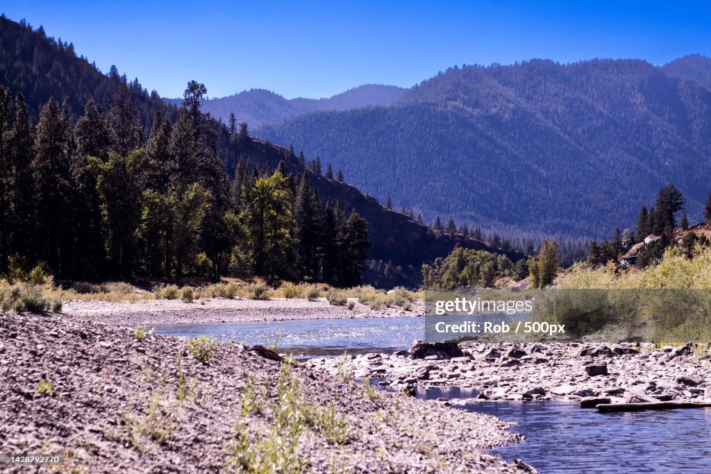 Scenic view of river by mountains against clear blue sky