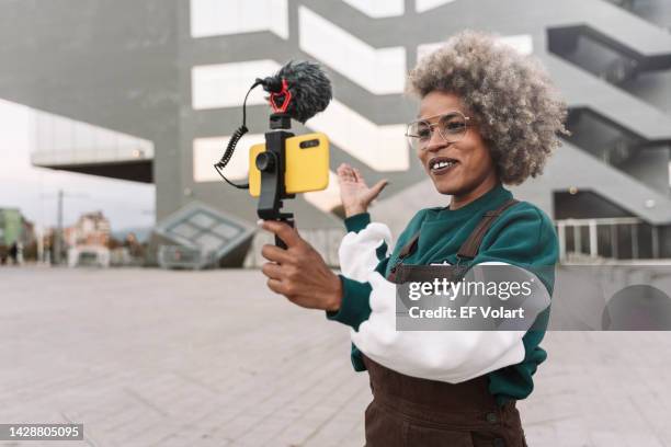 modern african american woman influencer recording a video vlog with smartphone in the city for online streaming apps - side hustle stock pictures, royalty-free photos & images