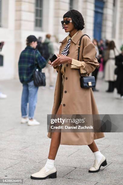 Guest is seen wearing a tan trench coat, Givenchy bag, Versace sunglasses and white and black shoes outside the Chloe show during Paris Fashion Week...