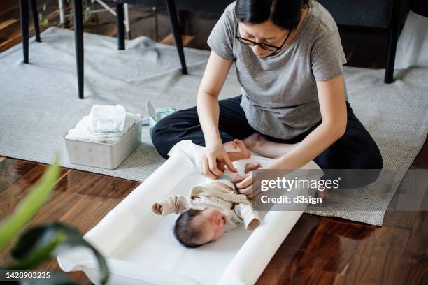 young asian mother changing the diaper for her newborn baby on the floor at home. new life. love and care concept - changing diaper ストックフォトと画像