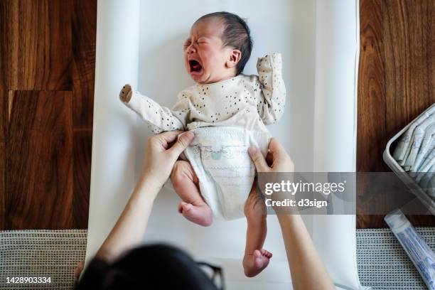 overhead view of mother changing the diaper for her newborn baby on the floor at home. new life. love and care concept - diaper change stock-fotos und bilder